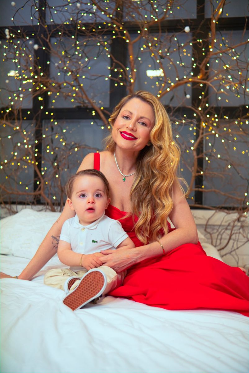 Mãe de vestido vermelho com o bebê no cenário de luzinhas